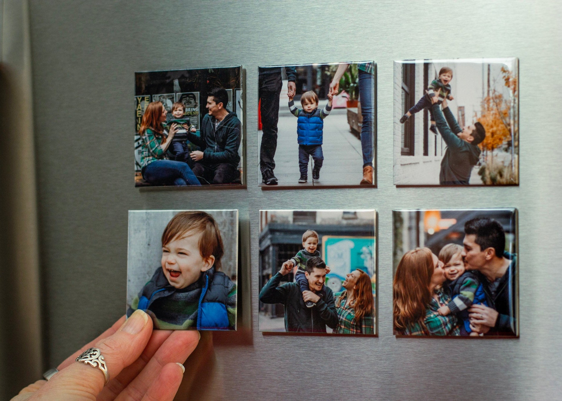 Hand placing a custom photo magnet on a refrigerator with a grid of family photo magnets